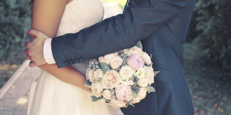 Beautiful sensual wedding couple and gentle bouquet of flowers, groom hugging lovely bride outdoors